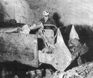 A miner loads a tram car with iron ore.