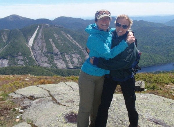 Carol Fox and Emily Lyons celebrate their ascent of Algonquin. The Trap Dike and the new slide on Mount Colden (the white one) can be seen in the background. Photo by Phil Brown