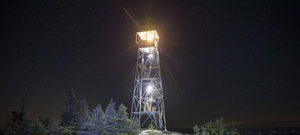 The fire tower cab was lit by a lantern. Hikers with headlamps can be seen climbing the stairs. Photo by Mike Lynch