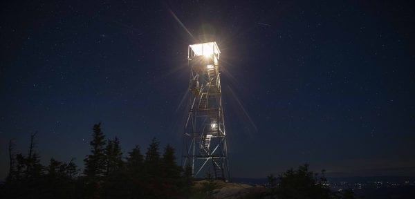 The fire tower cab was lit by a lantern. Hikers with headlamps can be seen climbing the stairs. Photo by Mike Lynch