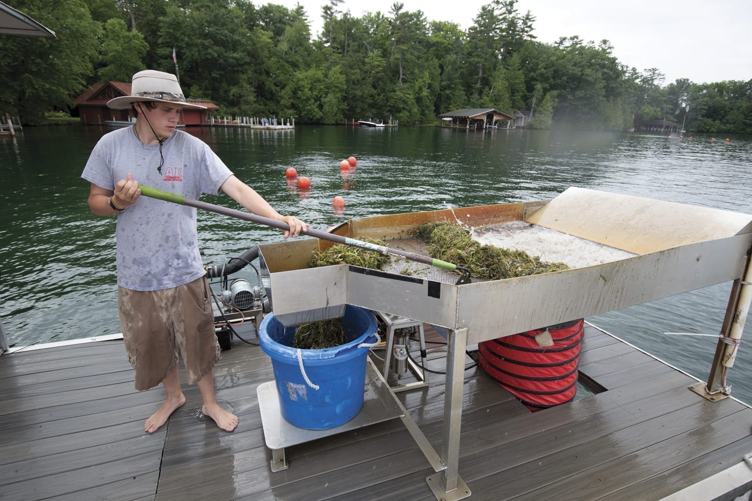 man on a boat uses a hoe to rake green plan matter around