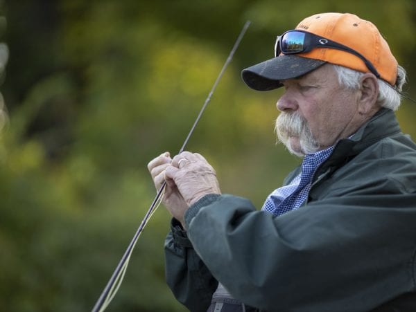 Rich Redman ties a fly on the shore along the Saranac River. Photo by Mike Lynch