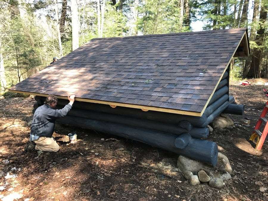 A crew member stains logs on the Kiwassa Lake lean-to.