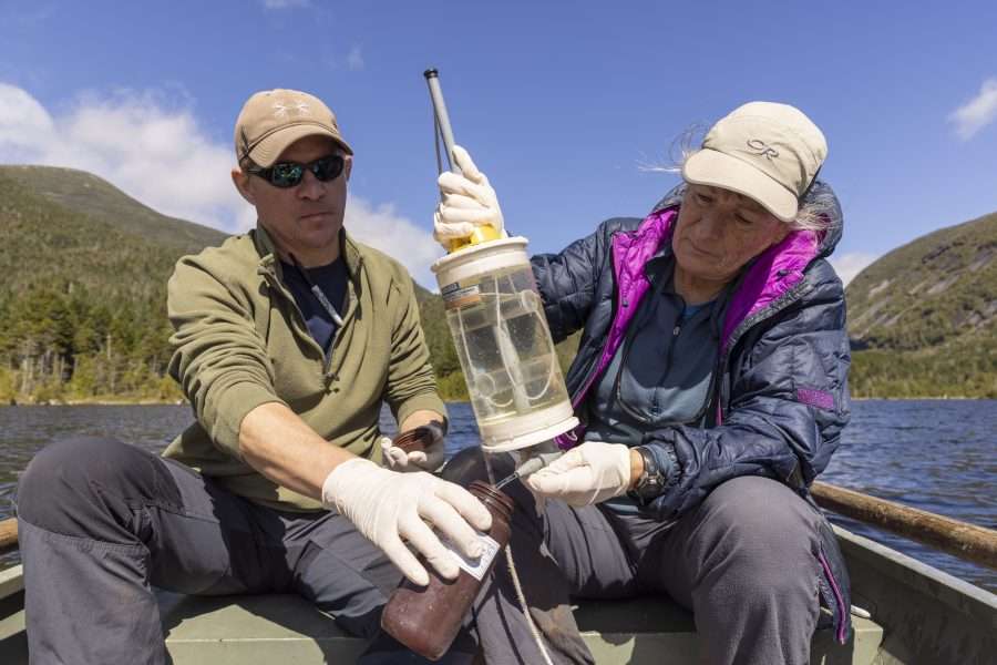 a man and a woman take a water sample from an adirondack lake as part of a lake monitoring project