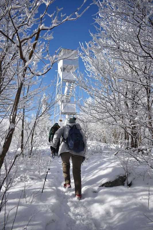 Doug & Susan Miller exiting a tunnel of snow-ladened trees as they approach a frosty Azure Mountain Fire Tower in early January.
