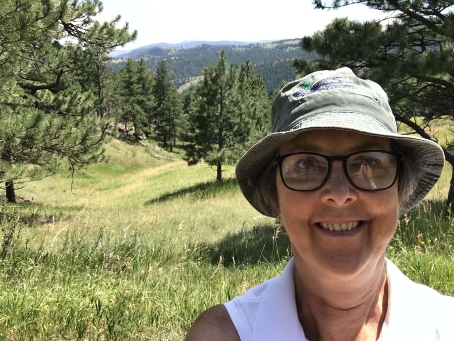 Long Lake Town Historian Hallie Bond stands in green grass with mountains behind her.