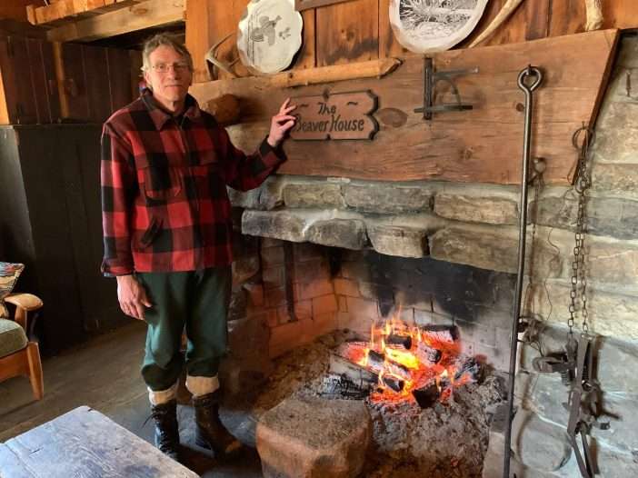 Dave Gibson wearing plaid shirt stands next to a fireplace