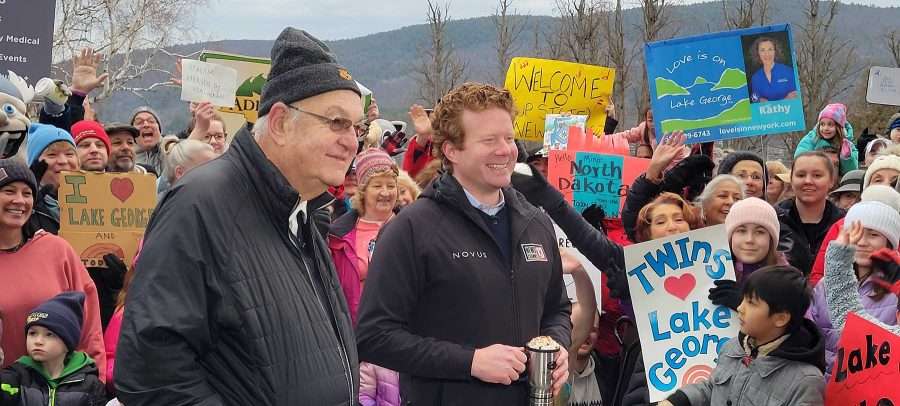 A crowd of people with an older man and a red-headed man in the foreground, both wearing black jackets. Robert Blais, in front, is believed to be the longest-serving mayor in United States. He's retiring at the end of March after 52 years in office