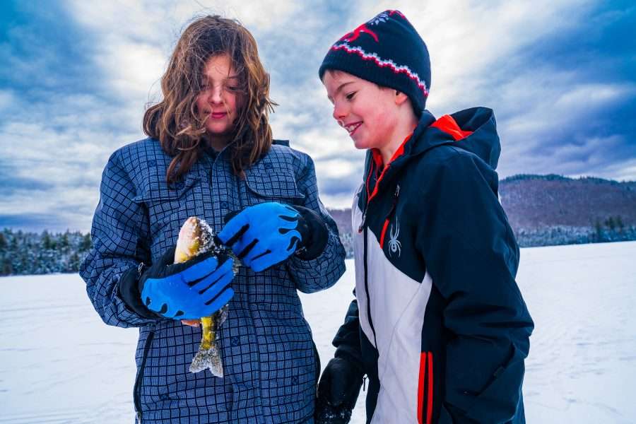 Two kids pose with a fish they caught while ice fishing