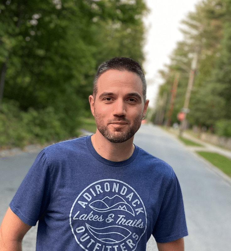 Climate change educator Joseph Henderson stands in a street lined with trees.