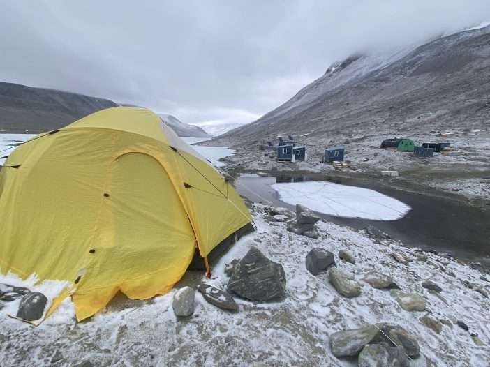A yellow tent sits near icy water bodies in Antarctica.