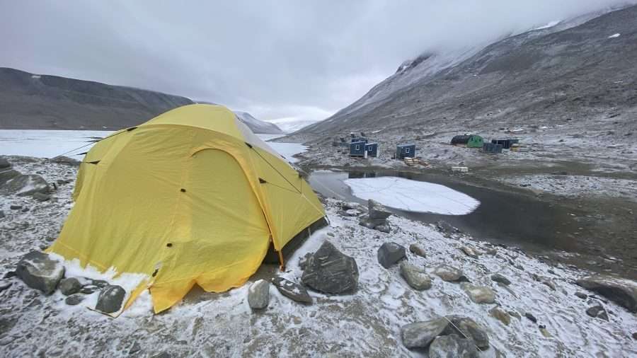 A yellow tent sits near icy water bodies in Antarctica.