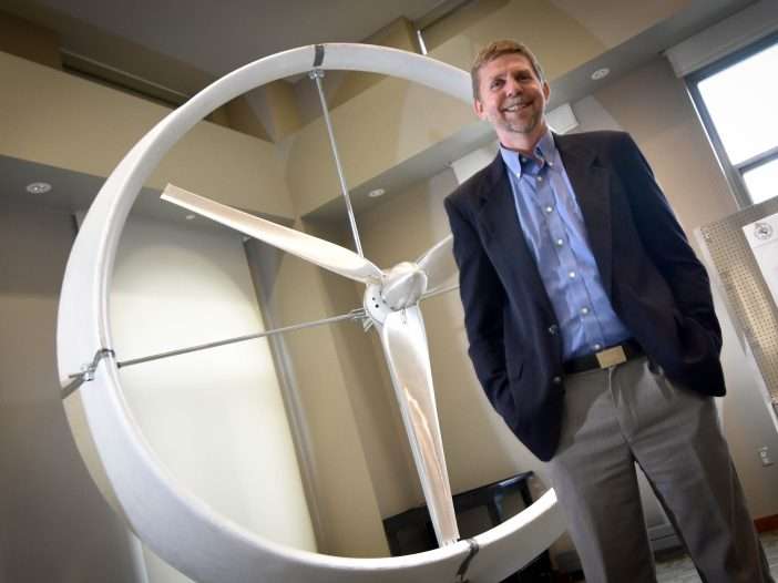 Ken Visser stands in front of a ducted windmill that is just a few feet taller than him.