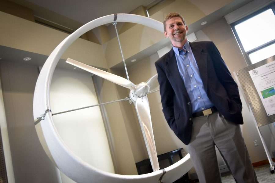 Ken Visser stands in front of a ducted windmill that is just a few feet taller than him.