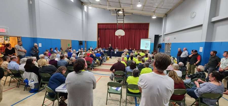 A large group of people gather in a school auditorium to discuss the installation of a battery storage facility.