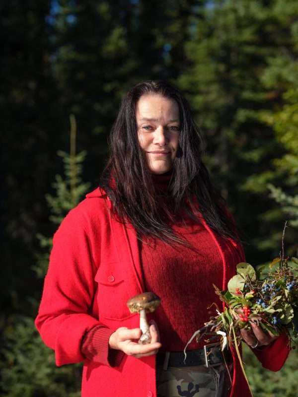 woman wearing red with foraged food, from the show 'Alone,' filmed in the canadian arctic