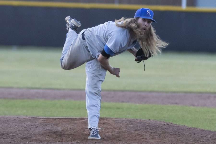 man with long hair throwing a baseball
