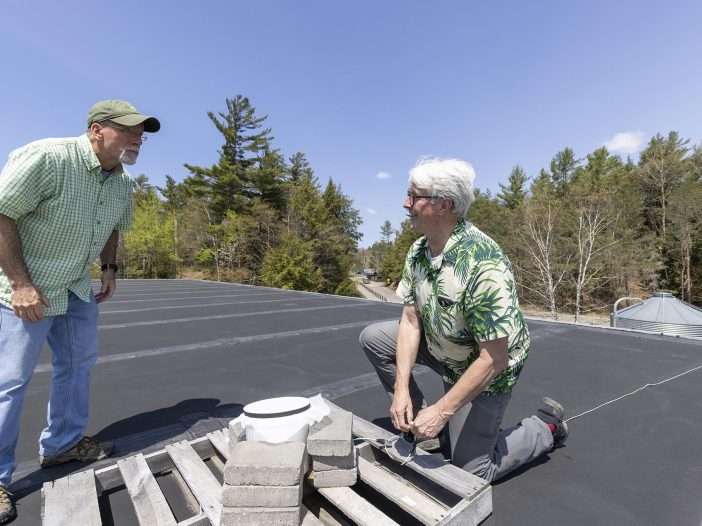 Adjunct professor Brian McAllister looks on as ornithologist Bill Evans, right, sets up a microphone on the roof of the science building at Paul Smith's College to capture bird call notes during nightime bird migrations. Photo by Mike Lynch