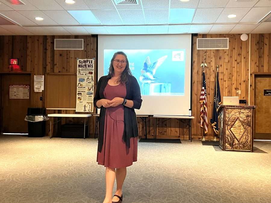 A woman talks in front of a projector screen with a bird on it