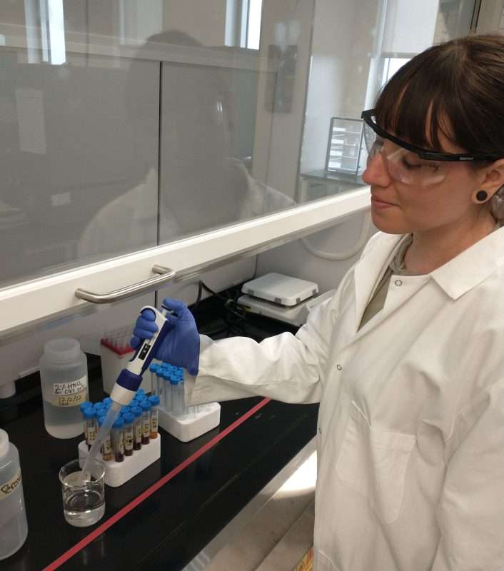A young researcher in a white coat uses a lab tool to study sediment cores.