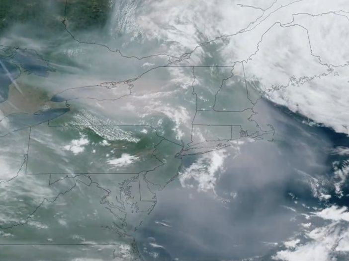 A blue, green and gray satellite image shows smoke blowing down from Canada.