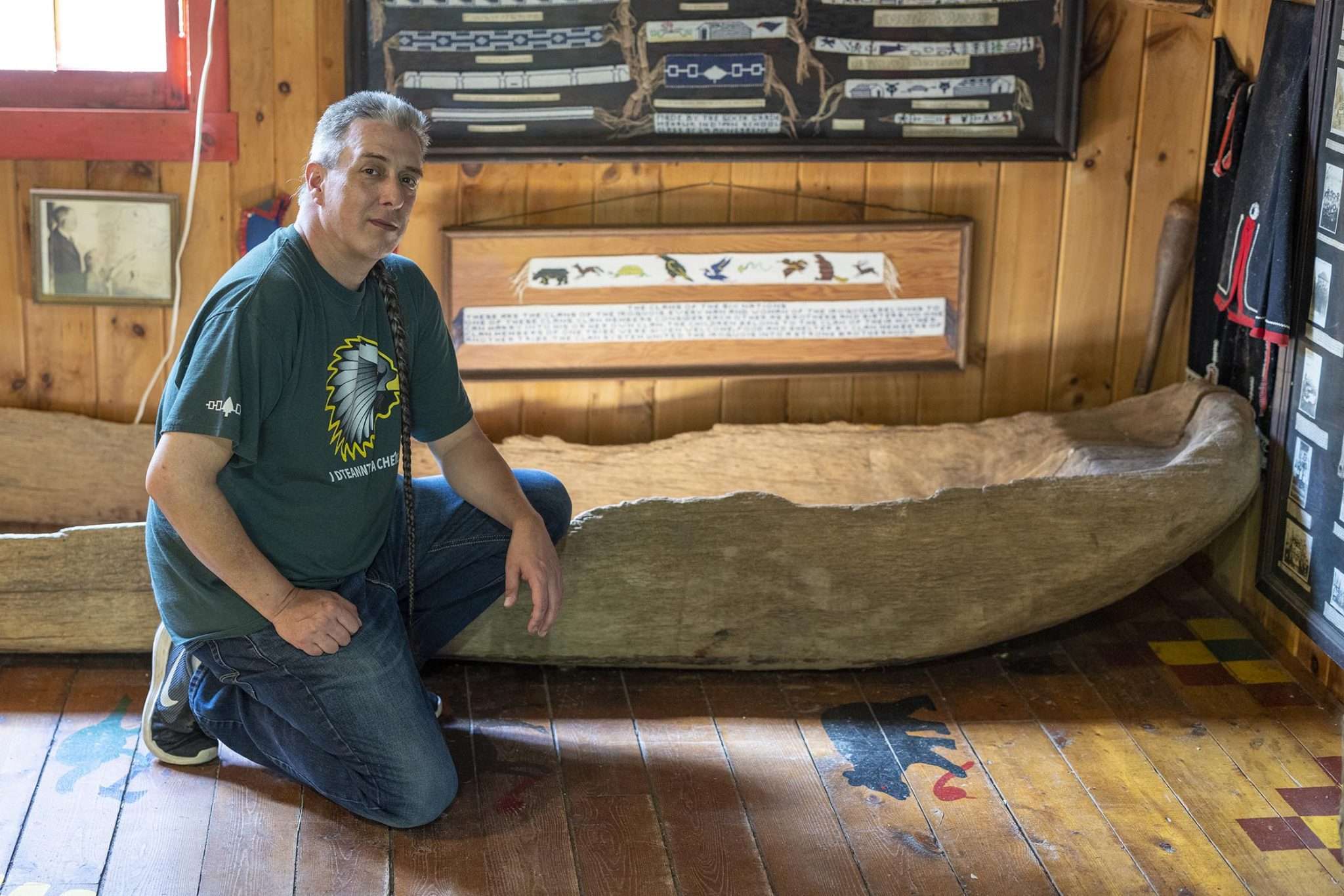 Dave Fadden, director of the Six Nations Iroquois Cultural Center in Onchiota, kneels next to a roughly 300-year-old dugout canoe that was found underwater in Lake Placid. His grandfather bought this artifact in the 1960s. It's unclear if it was made by Indigenous people.