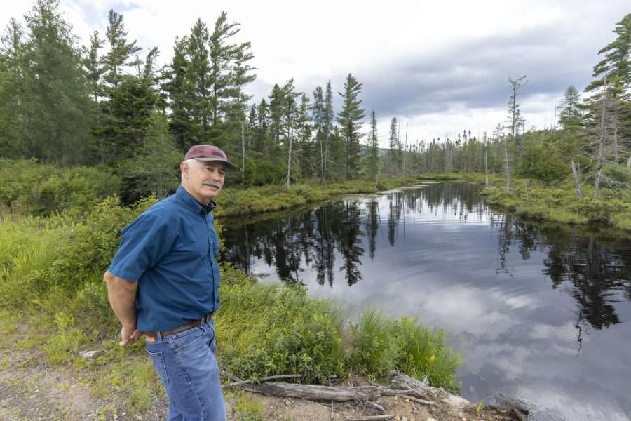 Chris Potter, the president of Brandreth Park Association, looks at the camera at a lake outlet in the Adirondacks.