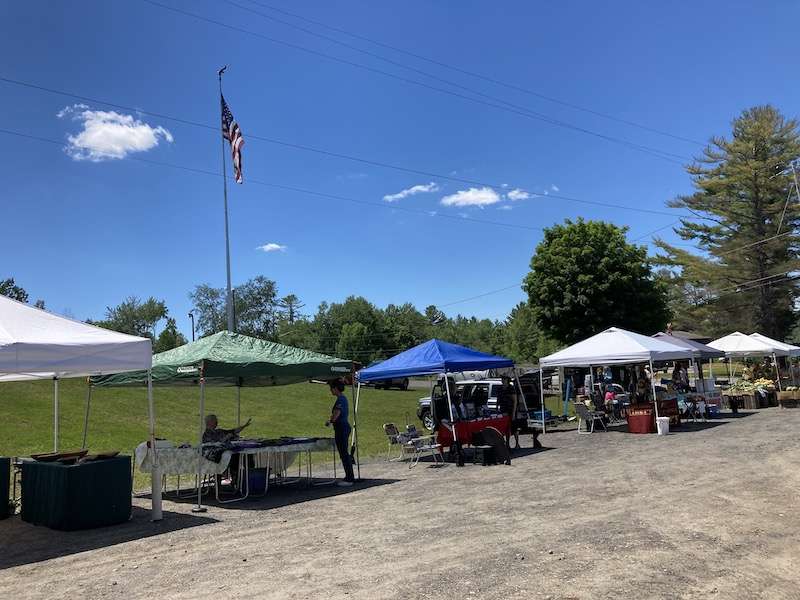 A clear sky and farmers market booths on a dirt road.