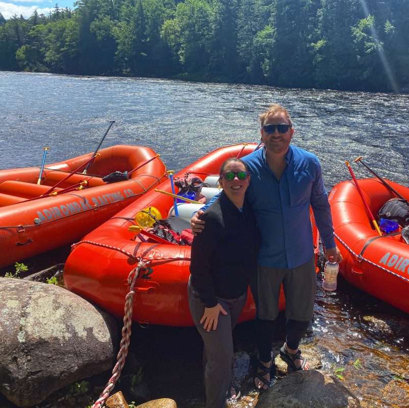 A couple poses for a photo while standing in a river during a sunny day.