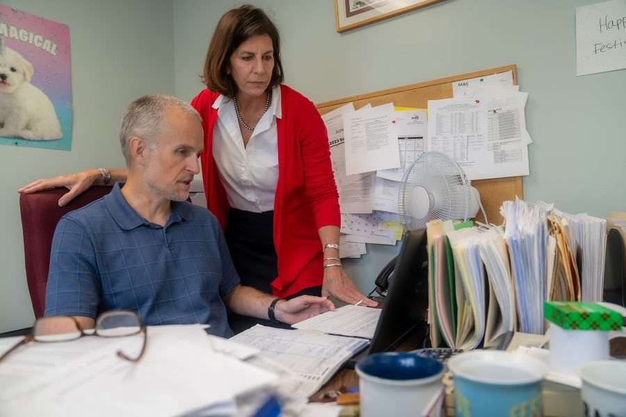 man at a desk and woman wearing red sweater standing behind him