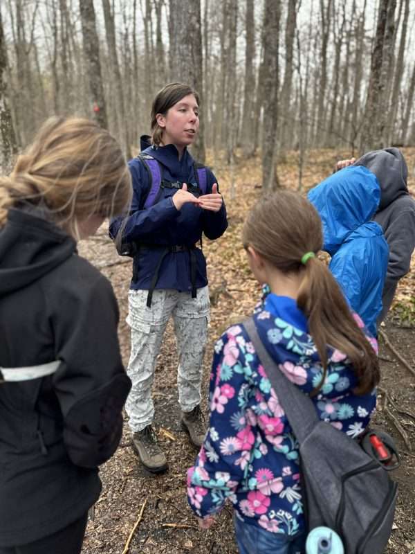 girl addressing group of kids in the woods