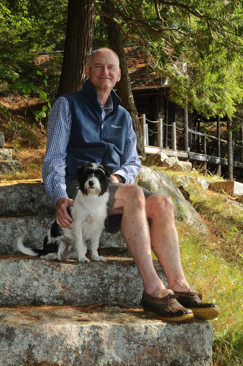 John Colston sits in front of his Long Lake camp, which is powered by solar and batteries