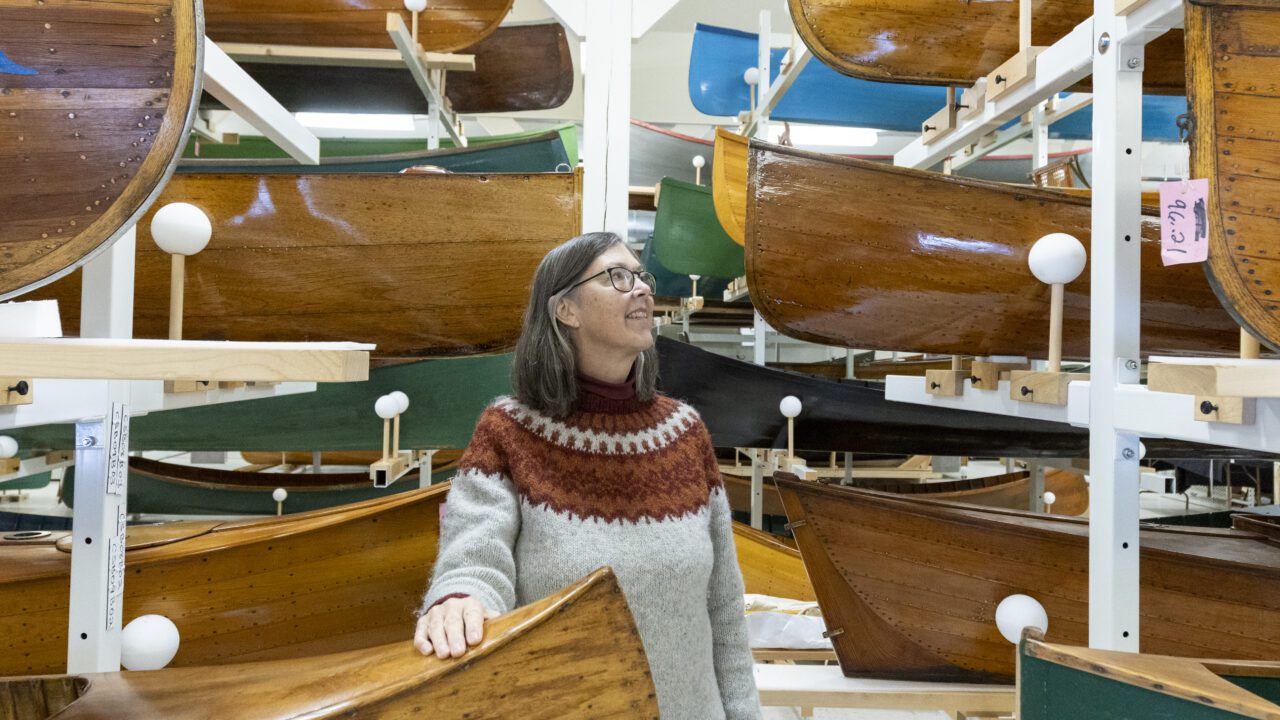woman standing among antique canoes