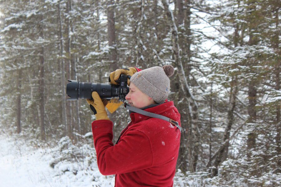 A photographer points a camera in a snowy forest.