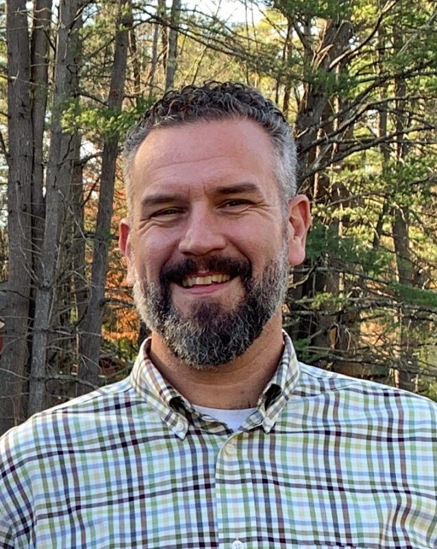 Man in button up shirt with trees behind him
