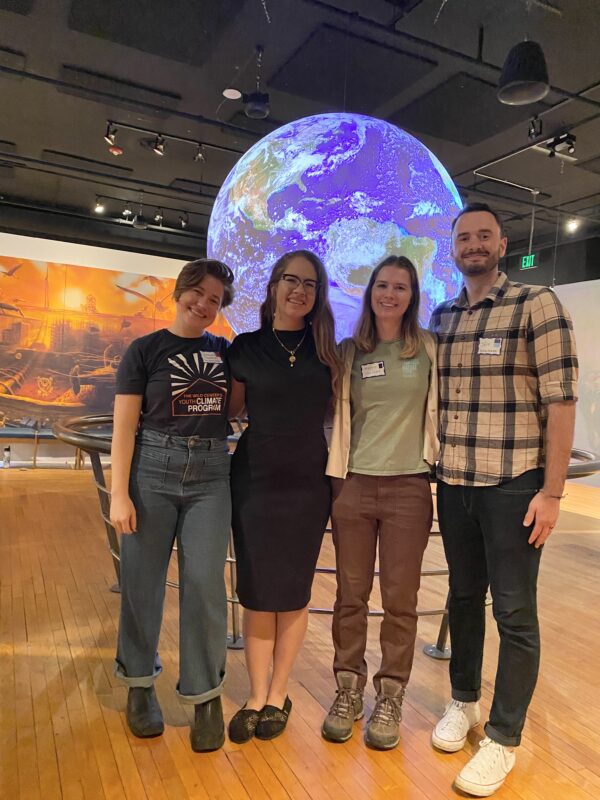A group working on environmental education stands in front of a lit-up globe.