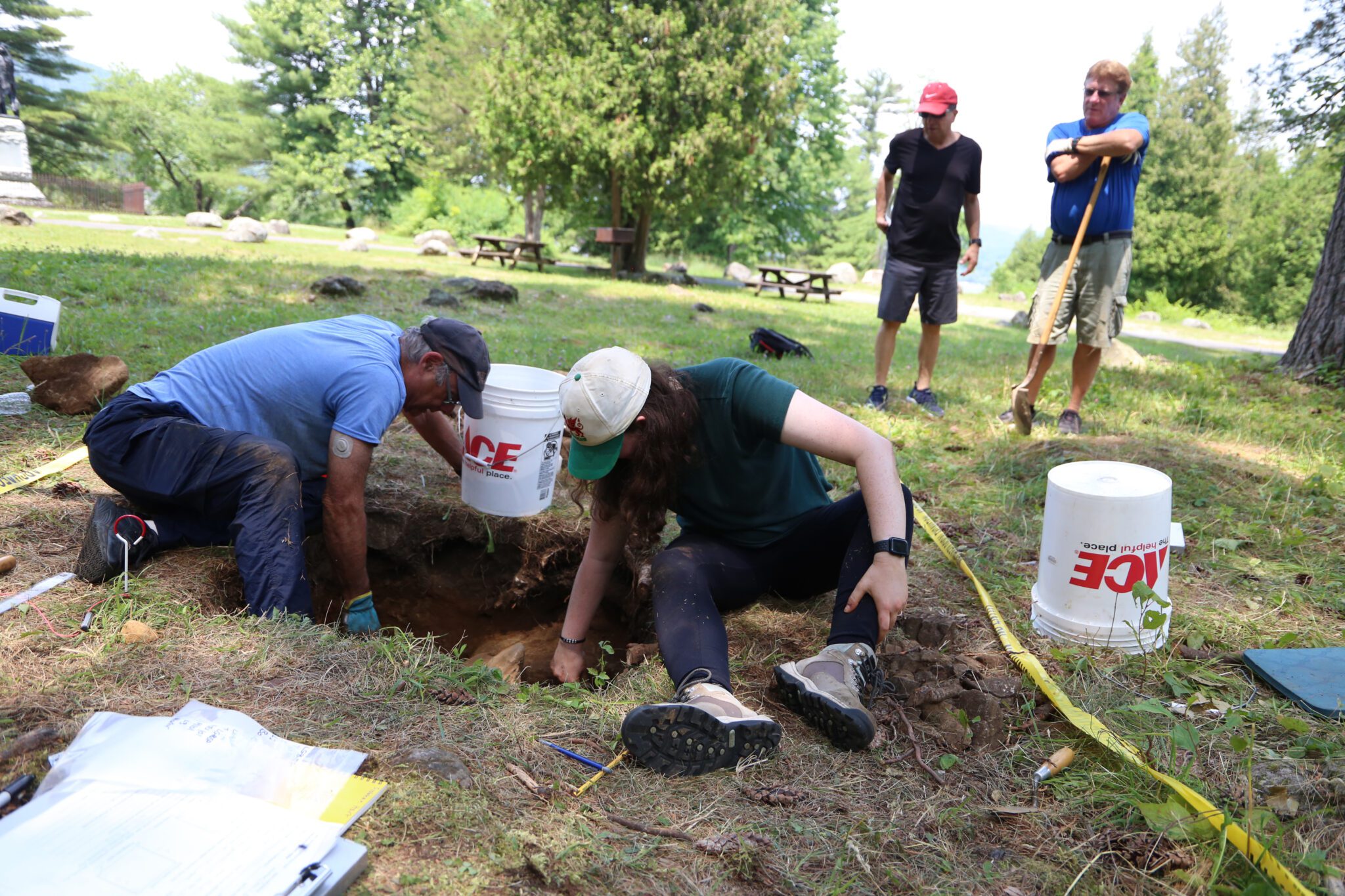 People dig in a test pit while two bystanders watch