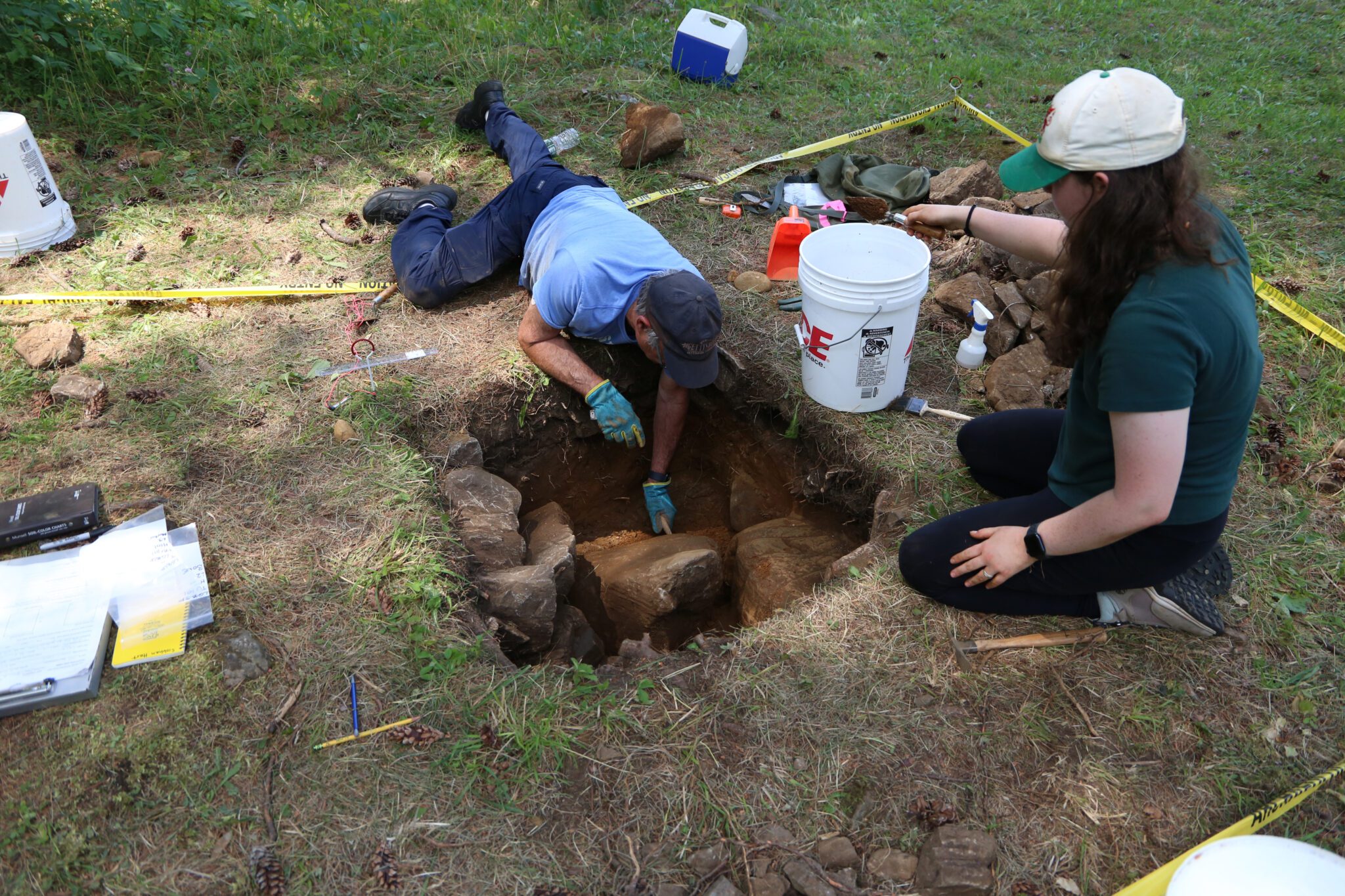 Two people examine an archaeological test pit 