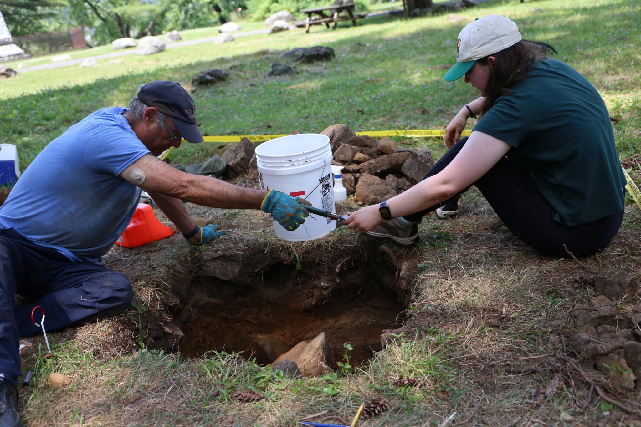 Two people examine an archaeological test pit at the Lake George Battlefield