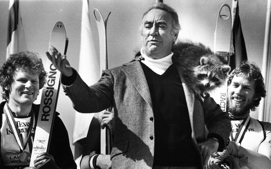 black and white photo of the opening ceremony for the 1980 Olympic Games in Lake Placid. Man gesturing with a racoon on his shoulder