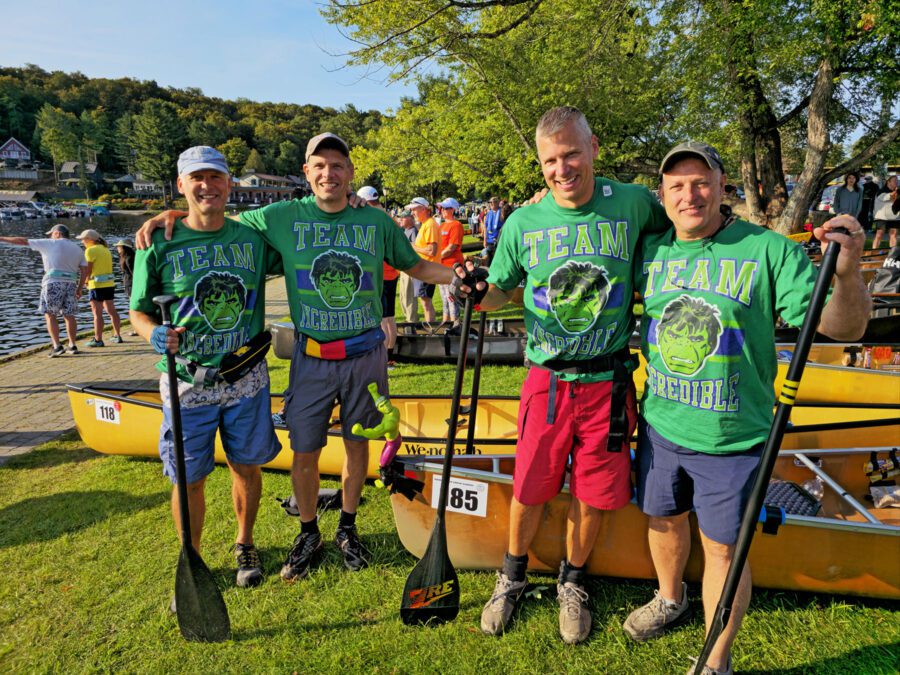 four guys in green shirts posing with canoe before the start of the 90-miler race