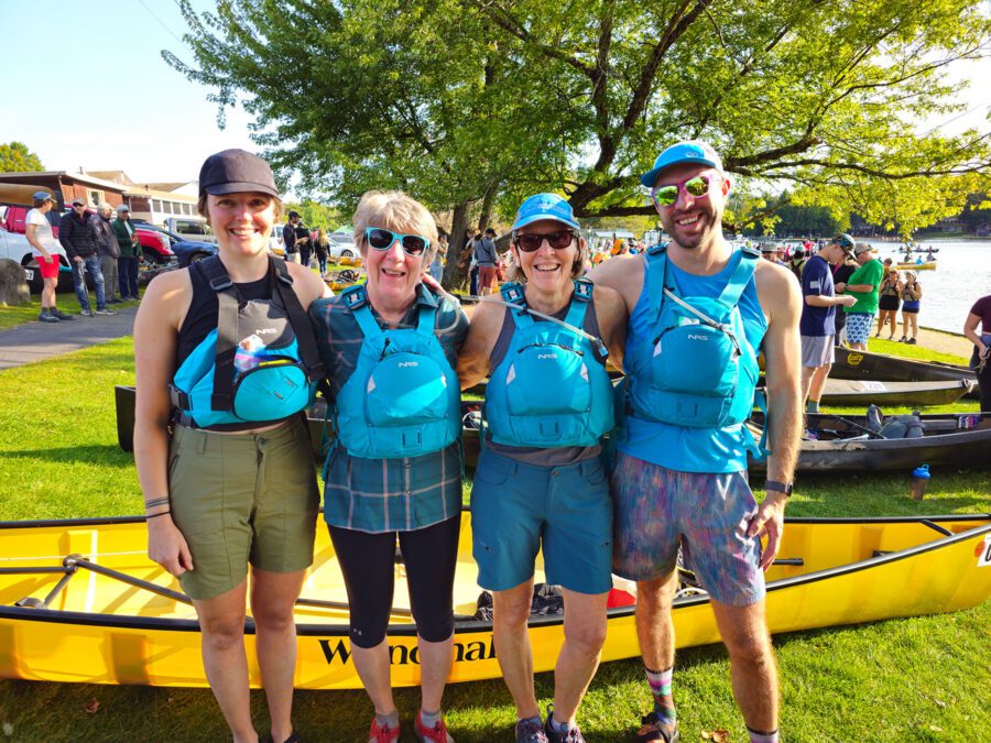 4 people in blue posing by canoe