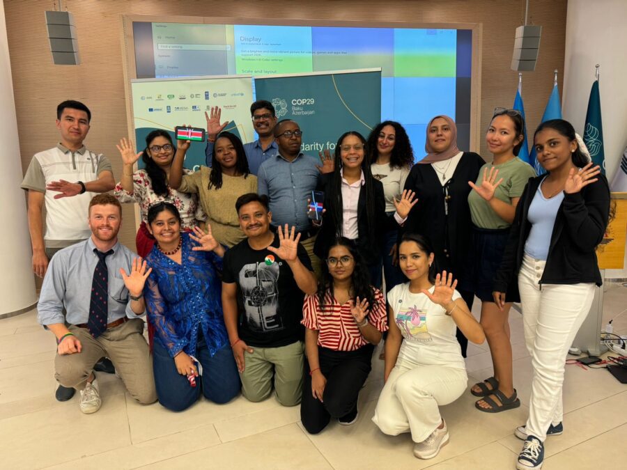 A group of teachers from across the globe wave to a camera.
