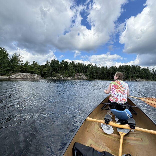 Woman in a tie-dye shirt paddling on a lake