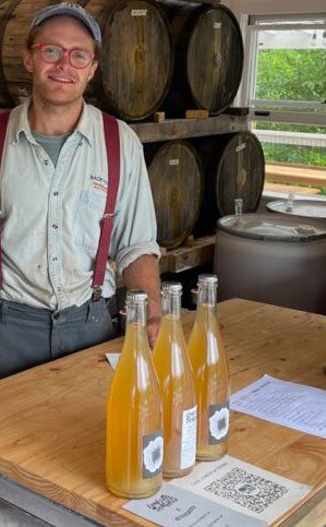 zach clemans of sandy's local cider standing in front of stack of barrels