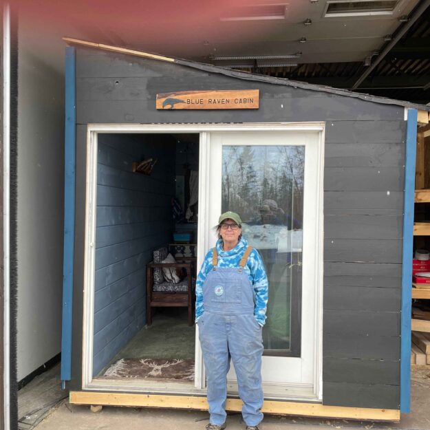 Deb Naybor stands outside of the Blue Raven Cabin. The tiny home is being built by Paul Smith's College students as a capstone project. Photo by Rick Karlin