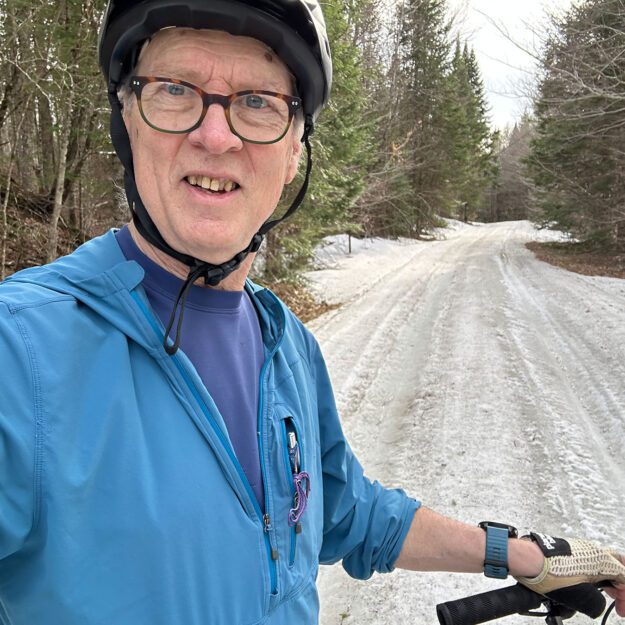 man wearing blue on a bike looking into the camera on an icy trail