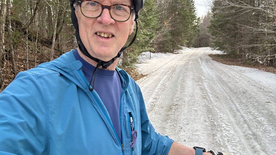 man wearing blue on a bike looking into the camera on an icy trail