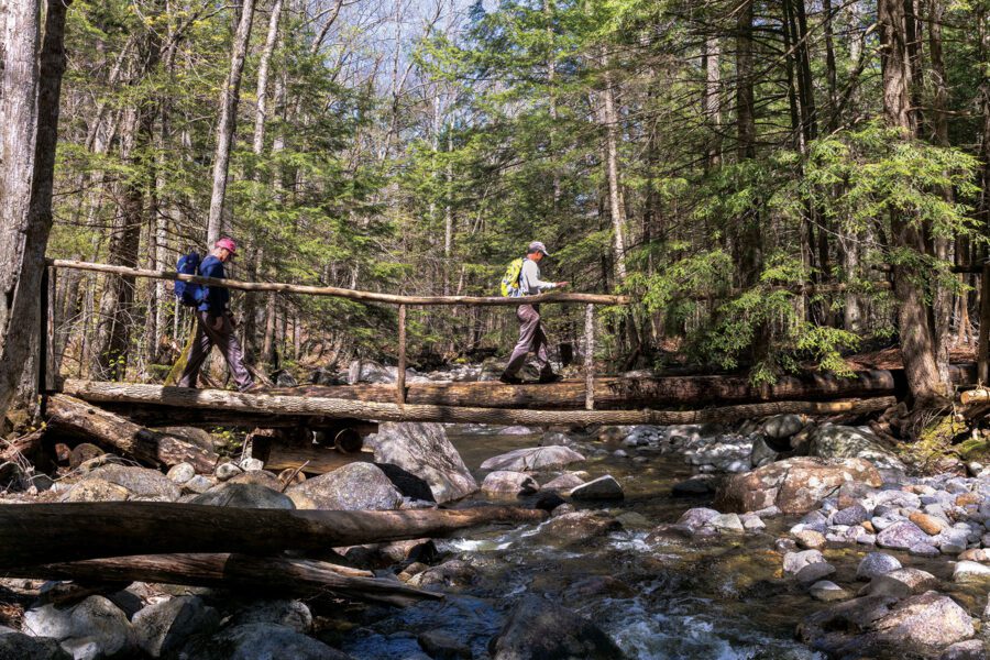 Two hikers cross a footbridge across Hoffman Notch Brook