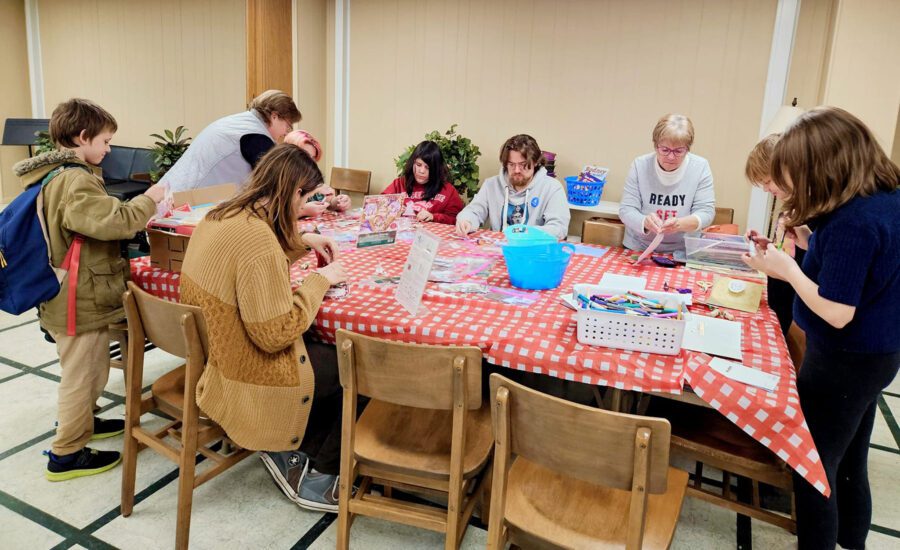 AmeriCorps members Zac Busch (front left, brown sweater) and Michael Rooney (seated behind table, gray sweatshirt) assist with Tupper Teens, an after-school program offering a space for teenagers to connect, explore interests, and participate in activities. The program is open to all teens in the community and is held on Wednesdays from 2:30 to 4:30 PM in the Community Room at the Tupper Lake Public Library.  Photo Courtesy of The Wild Center.


